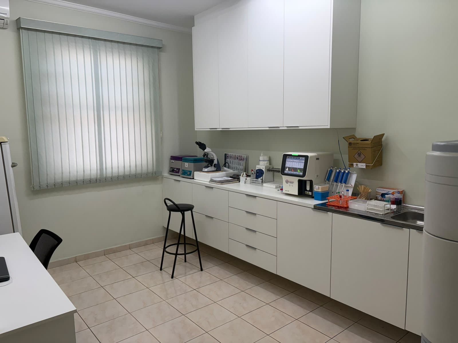 Bancada do laboratório com microscópio, analisador automatizado e material de coleta organizado